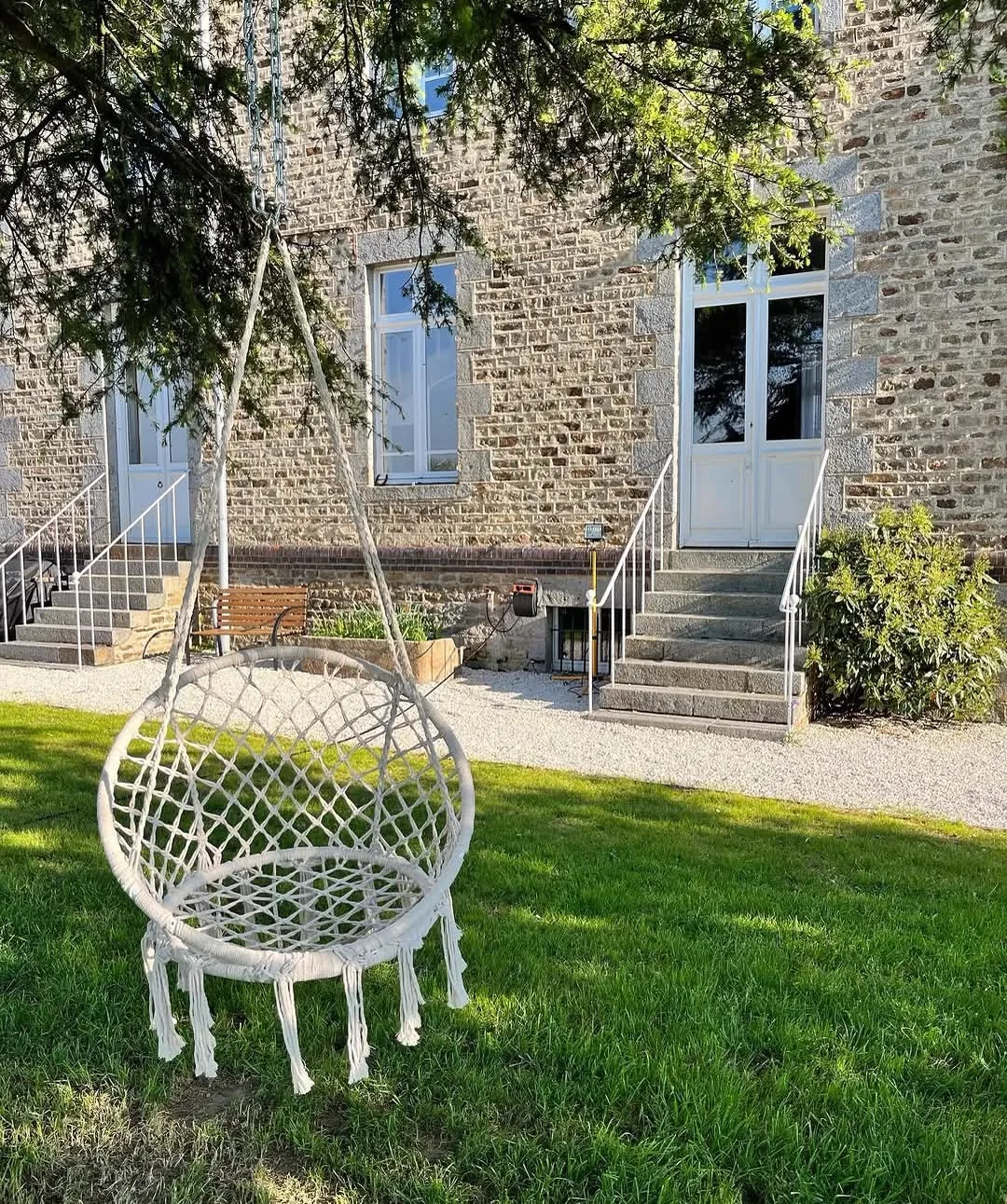 Hanging macramé chair on the lawn in front of the stone façade of Le Manoir Ducey