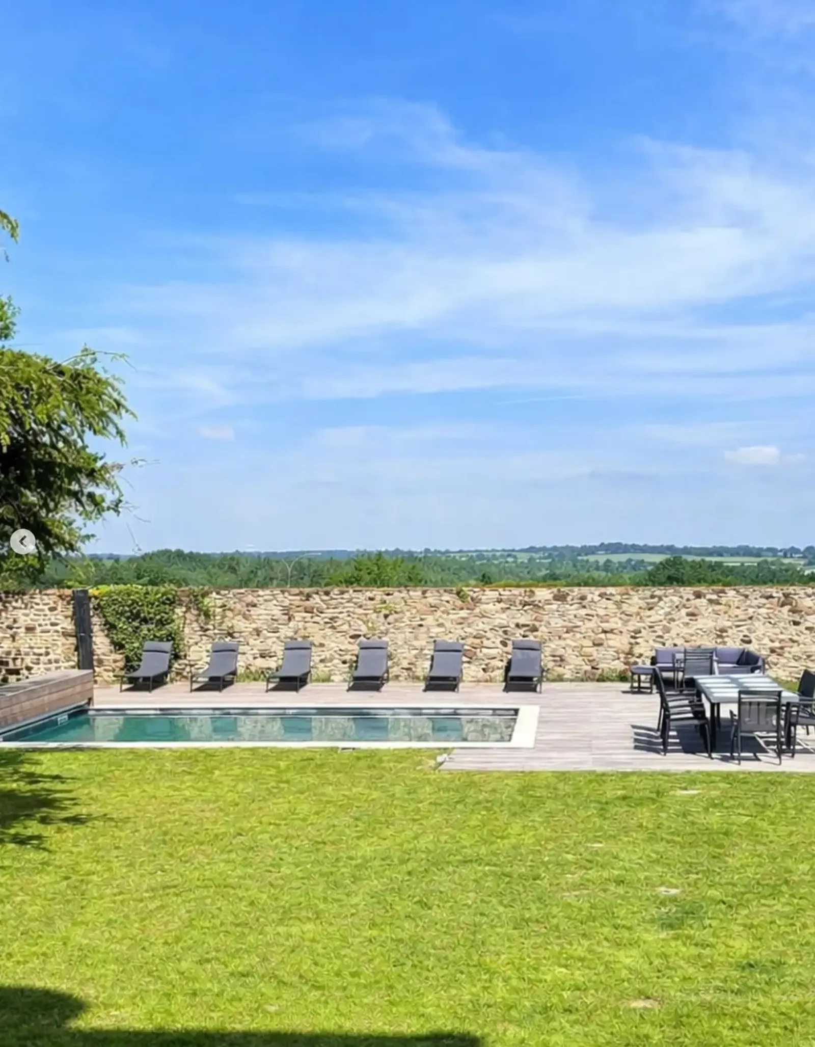 Heated swimming pool and lawn framed by the old stone wall, looking out over the Normandy countryside at Le Manoir Ducey